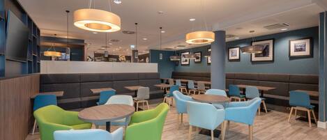 Un restaurante moderno con mesas redondas y sillas coloridas, iluminación empotrada y cuadros en las paredes.