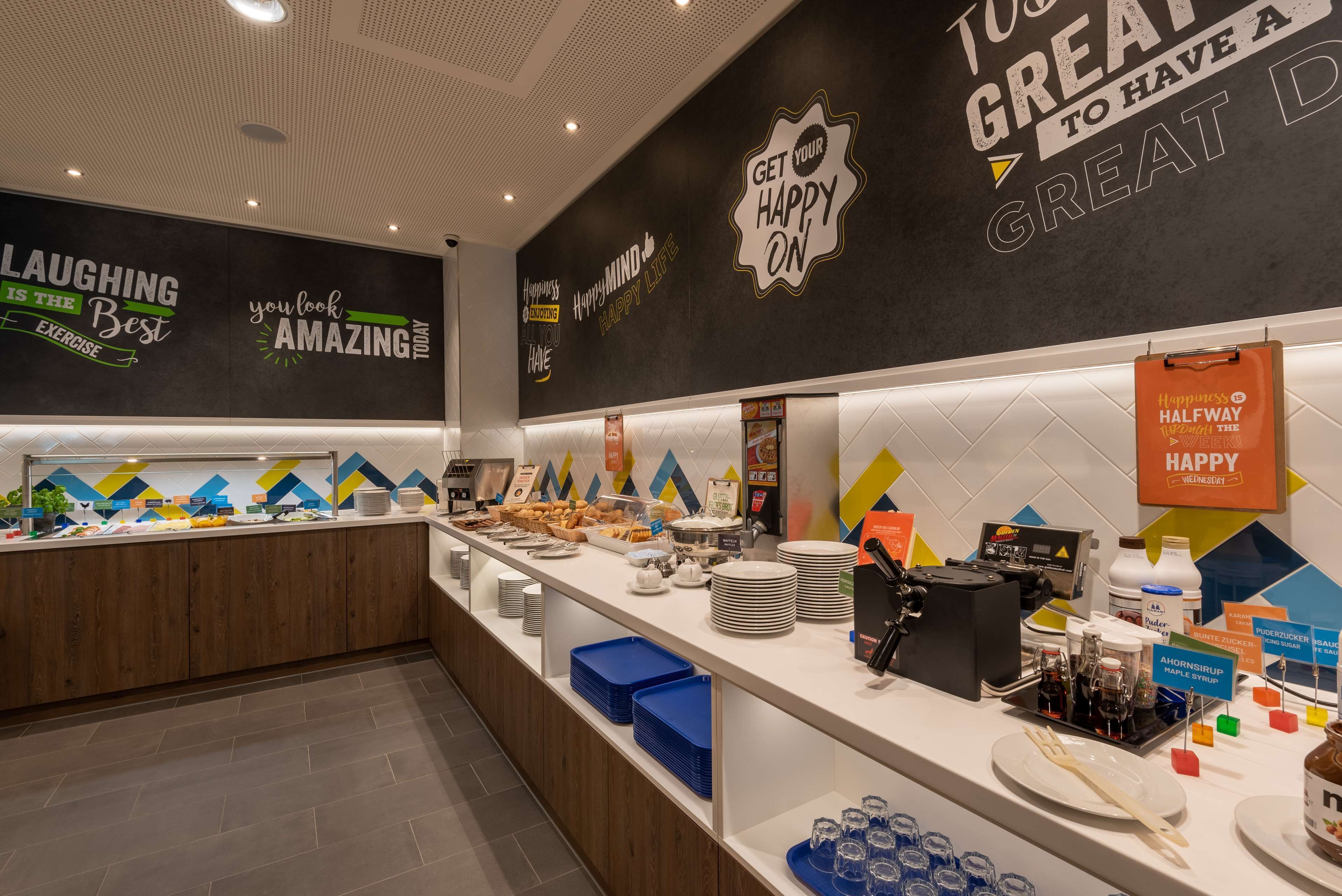 A buffet area with various food items and a motivational wall with phrases like "LAUGHING IS THE BEST EXERCISE" and "GET YOUR HAPPY ON".