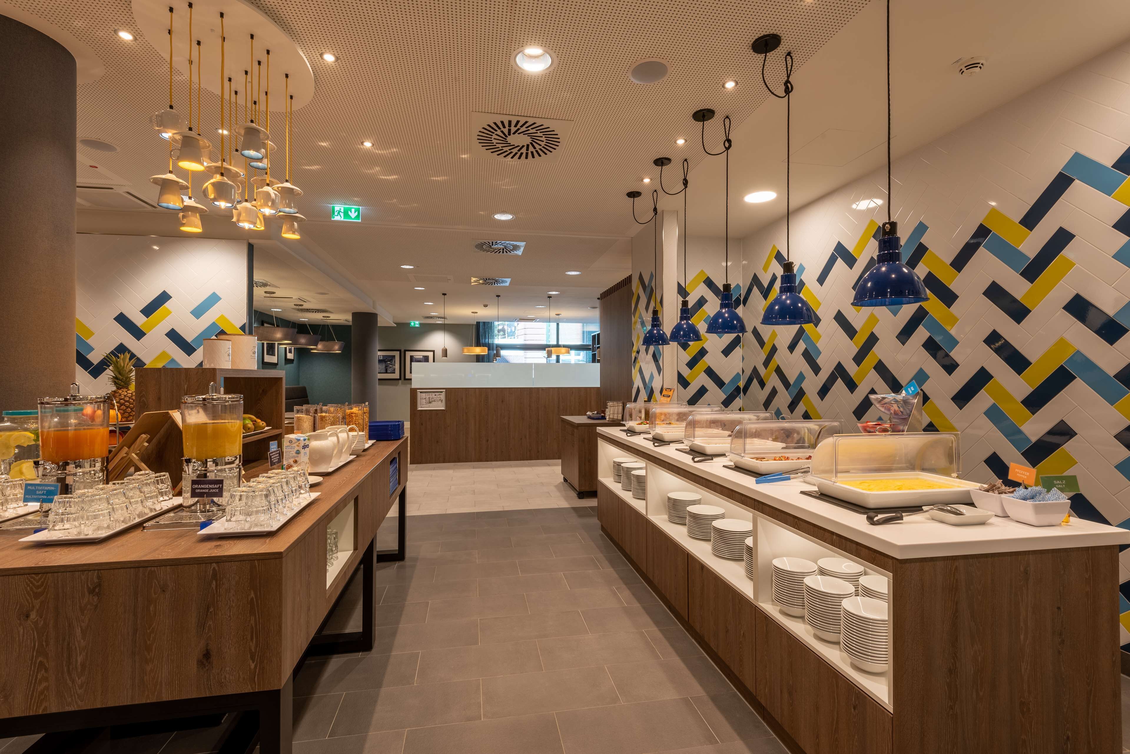 Un espace moderne dédié au petit-déjeuner, avec un long comptoir, une variété d'aliments pour le petit-déjeuner et un mur décoré de motifs.