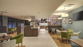 Un moderno vestíbulo de hotel con una zona de bar central, espacios de asiento y una recepción.