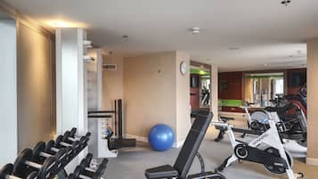 Un gimnasio con equipamiento de ejercicio, una pelota de ejercicios azul y una bicicleta de spinning para cardio.