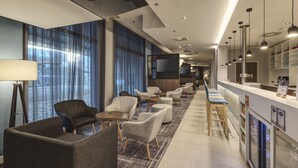 Una hall moderna di un hotel, con zone salotto, una reception e un bar.