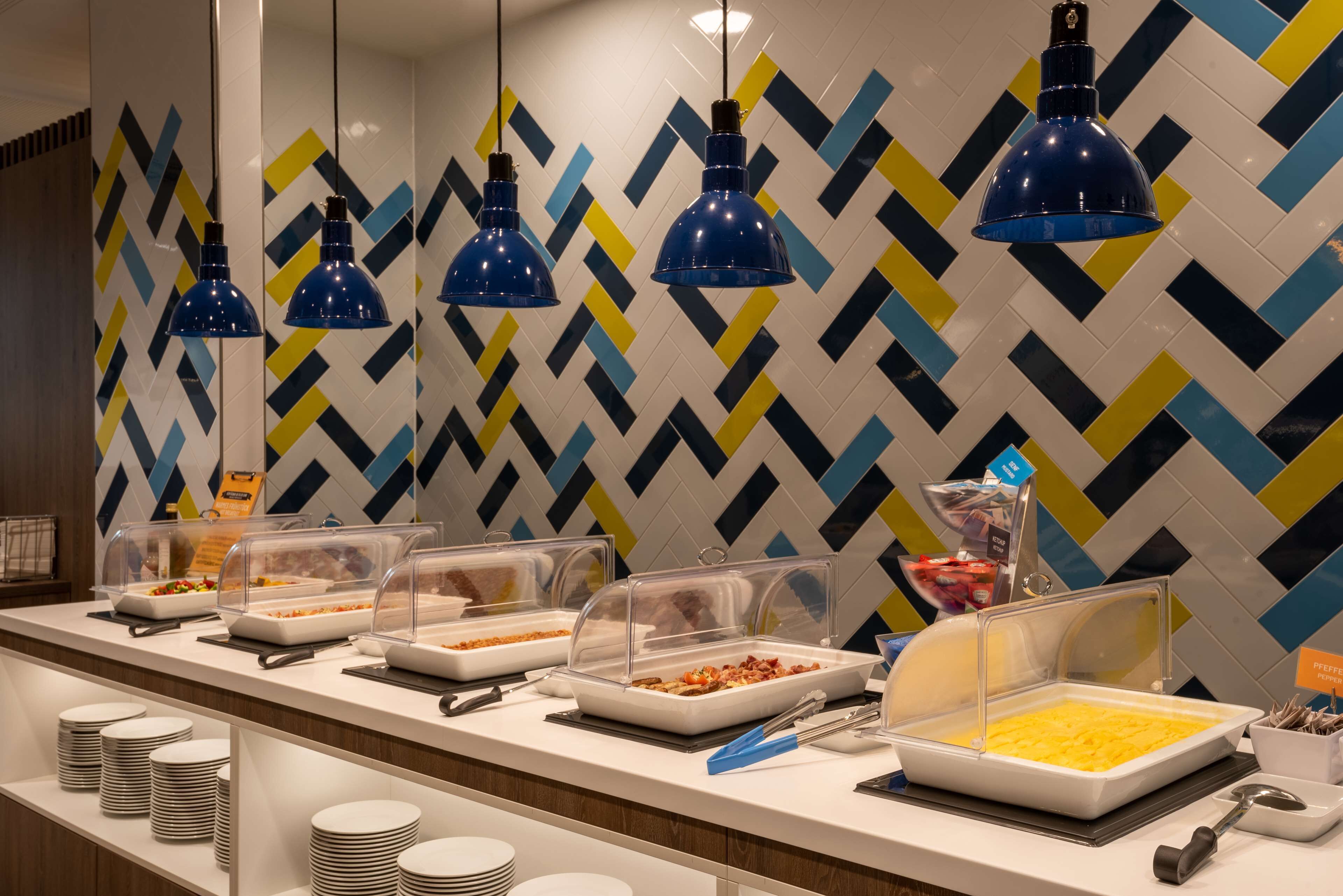 Montaje de bufé con varias estaciones de comida, vajilla transparente y un papel tapiz decorativo al fondo.