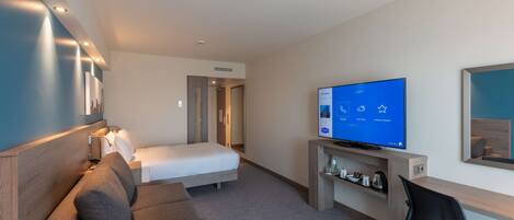 Ein modernes Hotelzimmer mit Bett, einer Couch, einem Schreibtisch, einem Fernseher und einem Spiegel.