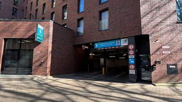 Un hôtel à plusieurs étages, avec une façade en briques, un panneau indiquant l’emplacement du parking et une entrée pour les piétons.