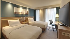 Camera d'albergo con due letti, una scrivania con una sedia, una televisione e un quadro appeso al muro.