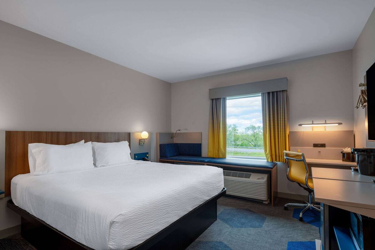 Ein Hotelzimmer mit einem großen Bett, einem Schreibtisch mit Stuhl, einem Fenster mit Vorhängen und Blick ins Freie.