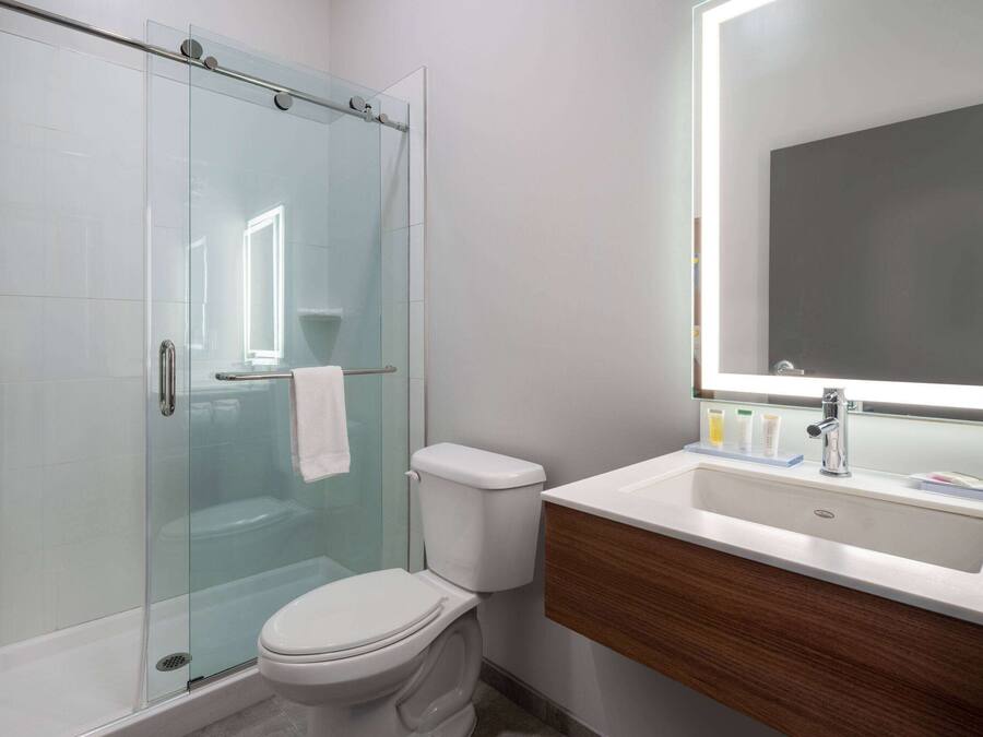 Ein modernes Badezimmer mit einer Duschkabine, einer weißen Toilette und einem Waschtisch mit Spiegel und Waschbecken.