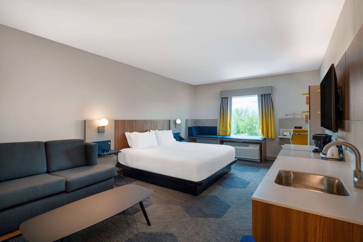 Ein Hotelzimmer mit Bett, Sofa, Schreibtisch, Waschbecken und einem Fenster mit Vorhängen.