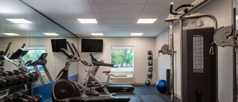 Un gimnasio con equipo de ejercicio, un espejo y una ventana.