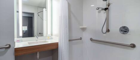 A modern bathroom with a shower, grab bars, a sink, and a mirror.