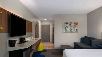 Een moderne hotelkamer met een flatscreen televisie, een bureau met koffiezetapparaat, een bank en een bed.