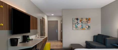 A modern hotel room with a flat-screen TV, a desk with a coffee maker, a sofa, and a bed.