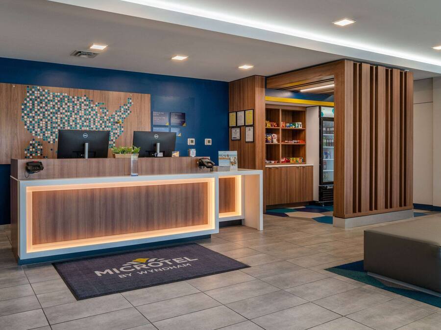 A hotel reception area with a wooden reception desk, two computers, a map of the USA on the wall, and a small plant on the desk.