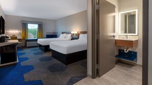 A hotel room with two beds, a desk, a chair, a desk lamp, a window with curtains, a bathroom with a mirror and sink. - Microtel Inn & Suites by Wyndham Winchester (Winchester)