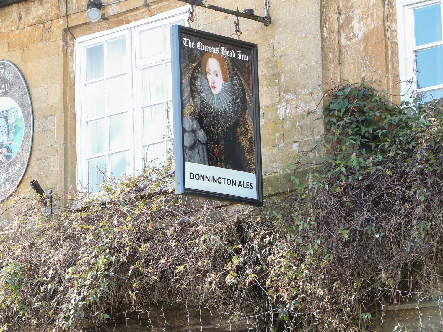 Une enseigne pour «The Queens Head Inn », avec un portrait et l’inscription «DONNINGTON ALES » en dessous.