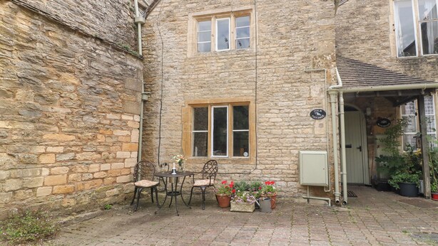 A stone cottage with a small patio, a table with chairs, and potted plants. - Coln Cottage (Cheltenham)
