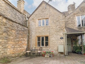 A stone cottage with a small patio, a table with chairs, and potted plants. - Coln Cottage (Cheltenham)