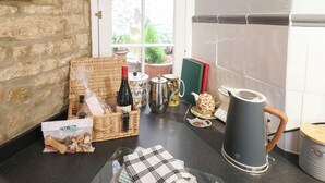A kitchen with a stone wall, a wicker basket, a wine bottle, a kettle, and a coffee maker. - Coln Cottage (Cheltenham)