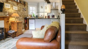 A cozy living room with a leather sofa, a fireplace, a stone wall, and a staircase leading to the upper floor. - Coln Cottage (Cheltenham)