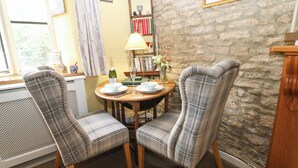 A dining area with two plaid chairs, a wooden table, and a stone wall. - Coln Cottage (Cheltenham)