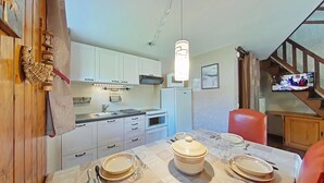 Une cuisine compacte avec des meubles blancs, une table à manger pour quatre personnes et un téléviseur fixé au mur.
