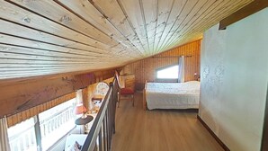 Une cabane en bois avec une chambre à coucher située en mezzanine, un petit coin repas et une vue sur l’extérieur.