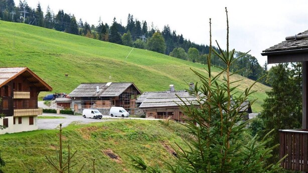 Un paysage rural avec des bâtiments en bois, une route et une colline verdoyante en arrière-plan.