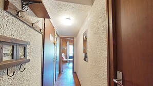 Un couloir avec une porte en bois sur la droite, un luminaire au plafond et une chaise au fond.