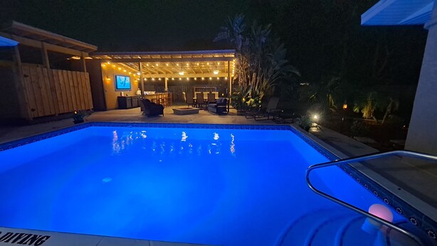 A swimming pool with a sunken hot tub, surrounded by lounge chairs and a covered seating area with string lights. - 3 bedroom private vacation home in merritt island (Merritt Island)