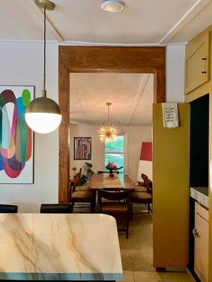 A modern dining area with a wooden table, chairs, and a chandelier. There is a painting on the wall and a sign on the door.