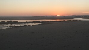 Ein Strand bei Sonnenuntergang mit ruhiger See und wolkenlosem Himmel.