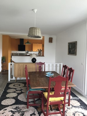 Un coin repas avec une table en bois et des chaises rouges, une cuisine en arrière-plan et un tapis à motifs sur le sol.