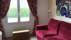 Ein Zimmer mit einem roten Sofa, einer Bank, einem Fenster mit Vorhängen und einem farbenfrohen abstrakten Gemälde an der Wand.