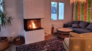 Ein gemütliches Wohnzimmer mit Kamin, einer Couch, einem gemusterten Teppich und einem großen Fenster.