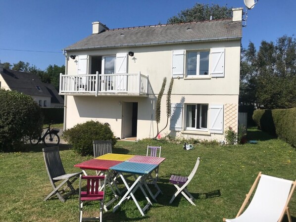 Une maison à deux étages avec un balcon, un petit jardin et du mobilier d’extérieur.