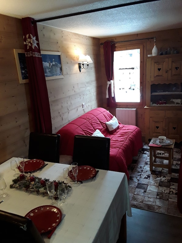 Une pièce chaleureuse avec un lit, une table à manger dressée pour deux personnes et une petite armoire en bois ornée de découpes en forme de cœur.