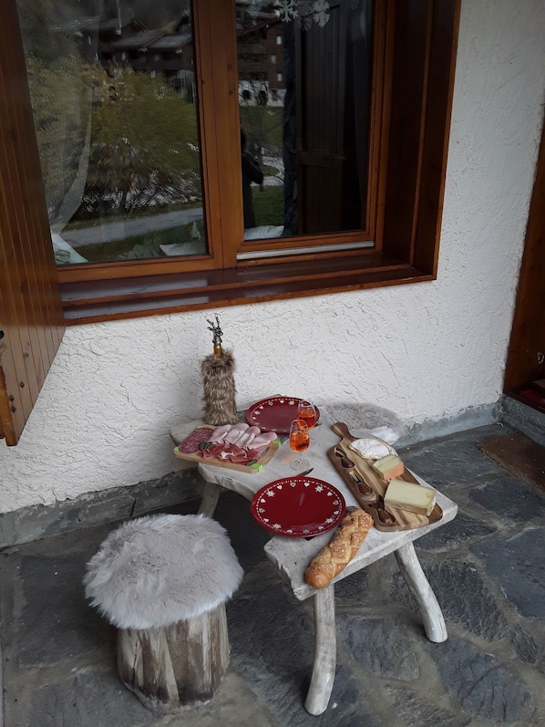 A table set with plates, glasses, and food items outside a building with a window.
