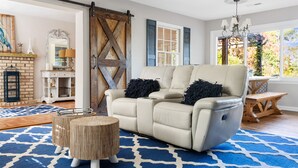 Una sala de estar con un sofá beige, un tapete azul estampado, una mesa de centro de madera y un ventanal con persianas azules.