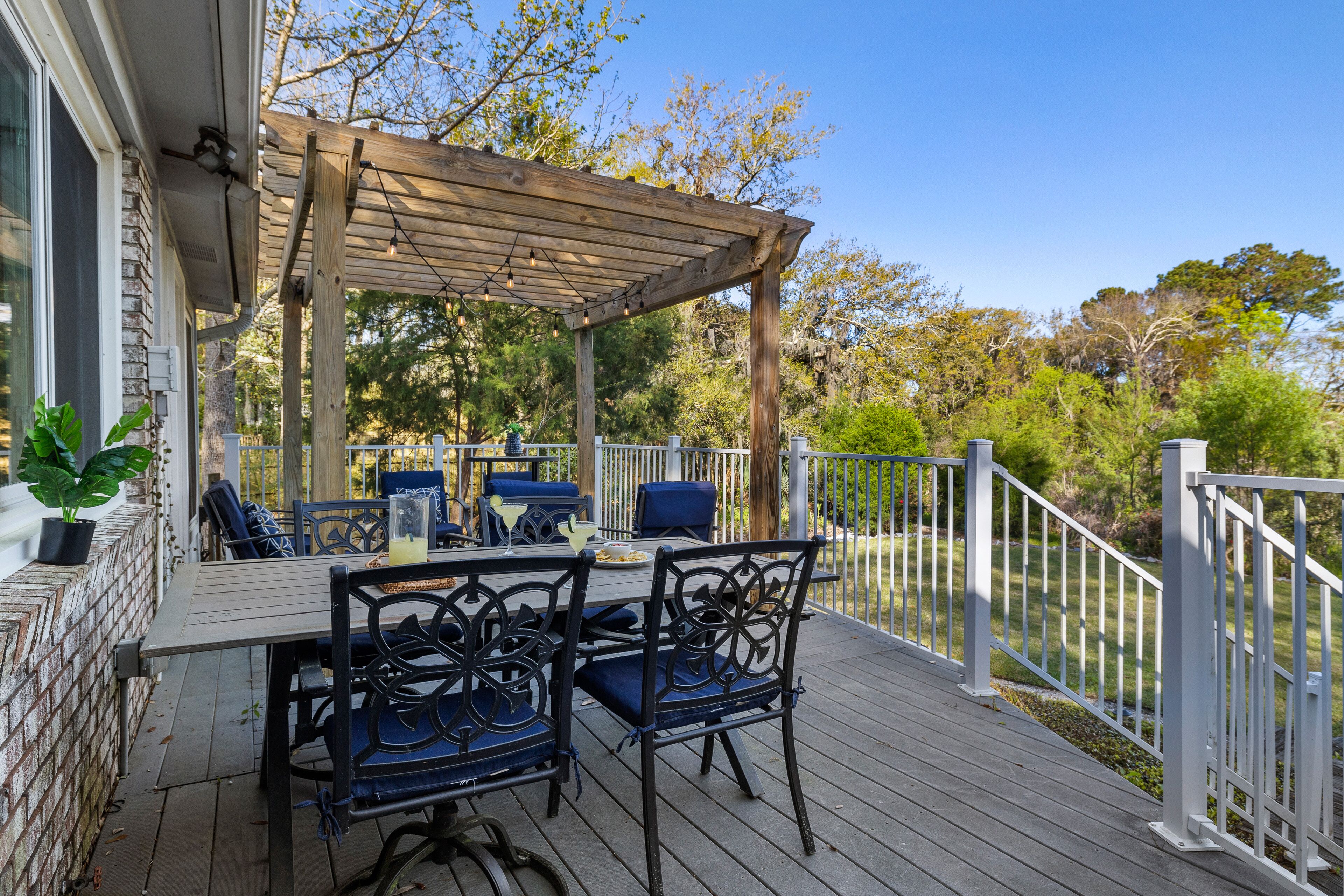 A covered outdoor patio with a table and chairs, surrounded by a wooden deck and white railing.