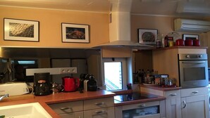 A modern kitchen with stainless steel appliances, a coffee maker, a red kettle, and framed pictures on the wall. - Charming duplex, 25m2 roof terrace in the center of the old village, wifi (Collioure)