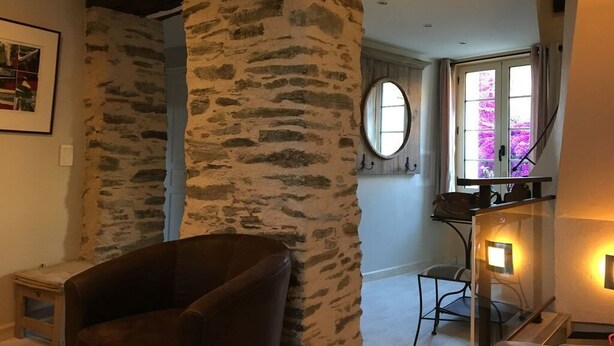A room with a stone wall, a brown leather chair, a small table, and a window with curtains. - Charming duplex, 25m2 roof terrace in the center of the old village, wifi (Collioure)