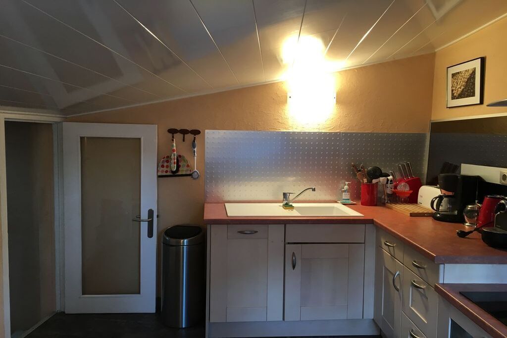 Cocina compacta con encimera blanca, un lavamanos y un cubo de basura de acero inoxidable.