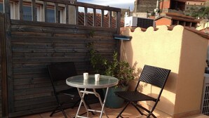 A small outdoor patio with a round table and two chairs, a potted plant, and a wooden fence. - Charming duplex, 25m2 roof terrace in the center of the old village, wifi (Collioure)