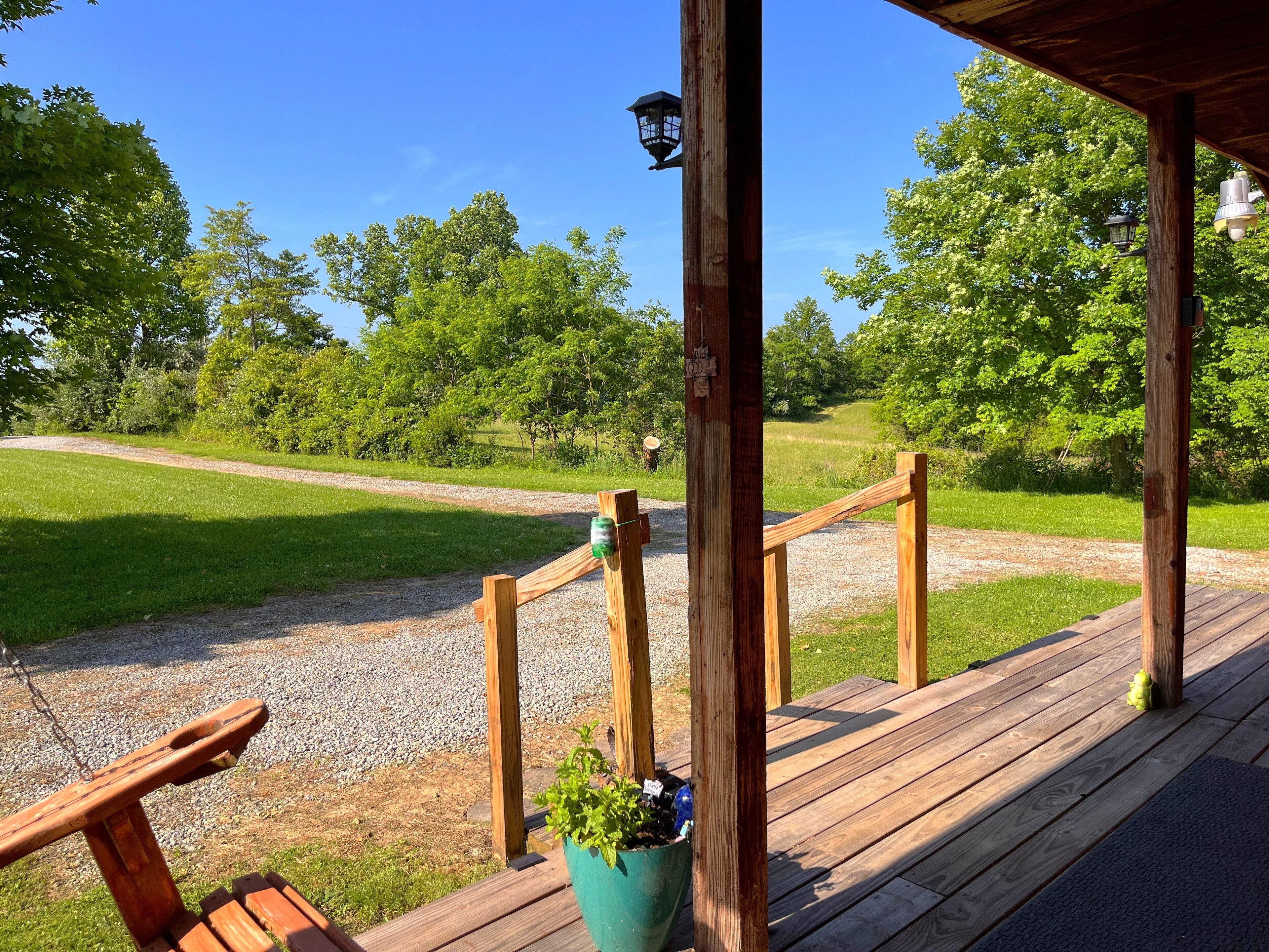 A wooden deck with a bench and a planter, overlooking a grassy area with trees.