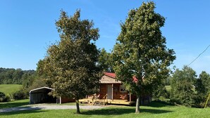 A rustic cabin with a red roof, surrounded by lush green grass and trees. - Beautiful country views and wildlife. Less than 2 miles from downtown. (Point Pleasant)