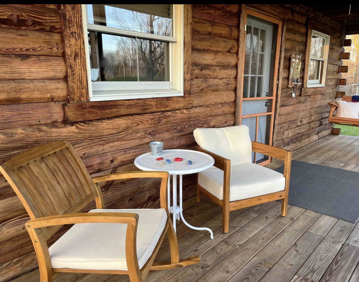 A wooden cabin with a porch featuring two wooden chairs and a small round table.