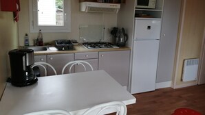 Cocina compacta con estufa a gas, pileta y microondas. Hay una mesa con sillas y un taburete rojo.