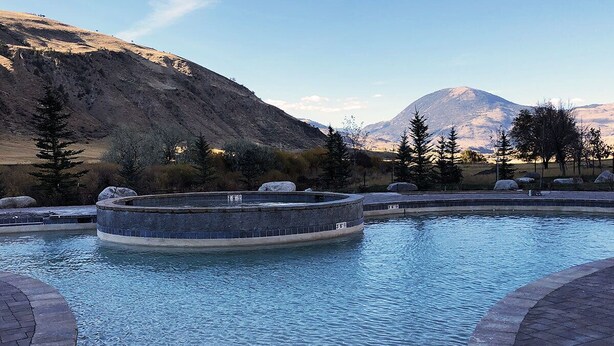 Una piscina circular con borde de piedra, rodeada de escalones de piedra y un telón de fondo montañoso.