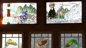 Una ventana de vitral con una escena de montaña y un árbol.